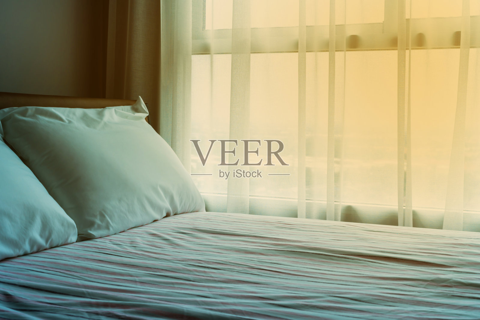 柔软的床上放着白色的枕头，粉色的床单和橙色的灯照片摄影图片