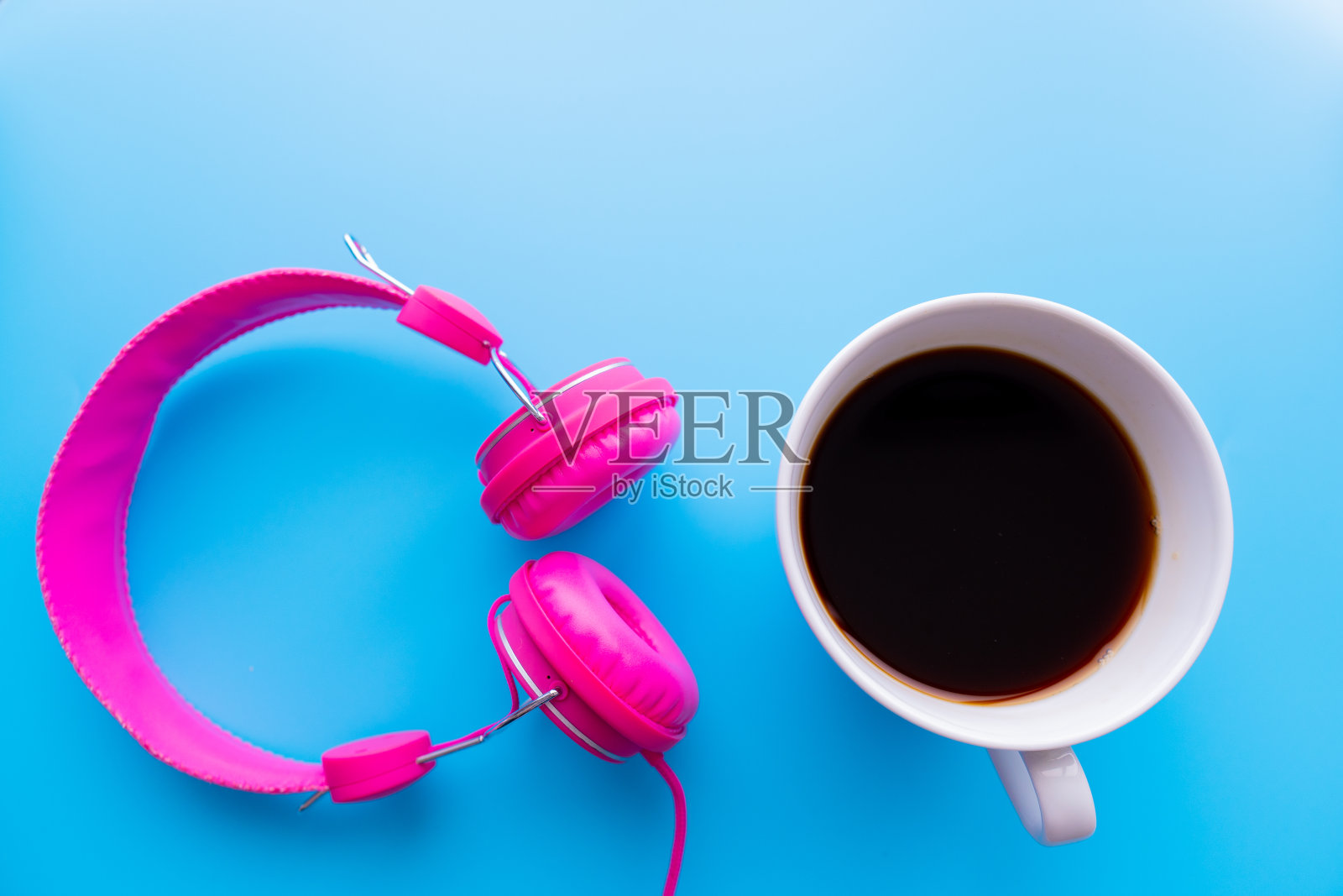 俯视图的咖啡杯是听音乐的粉红色耳机上的蓝色背景与复制空间。照片摄影图片