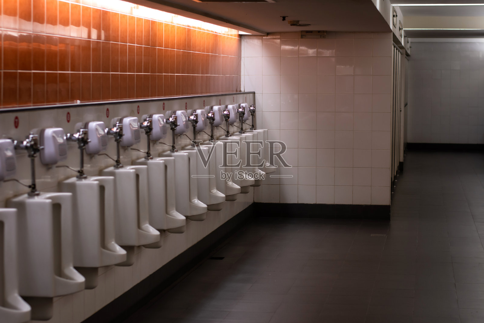 公共男厕墙上白色小便池，光线较暗。照片摄影图片