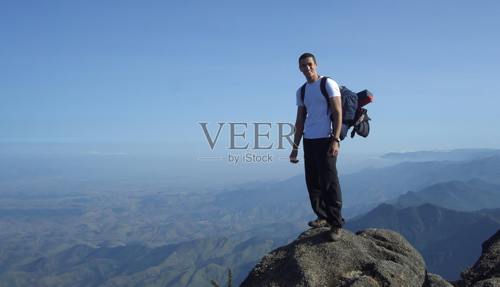 一个背着大背包的男人在山顶上看着摄像机。照片摄影图片