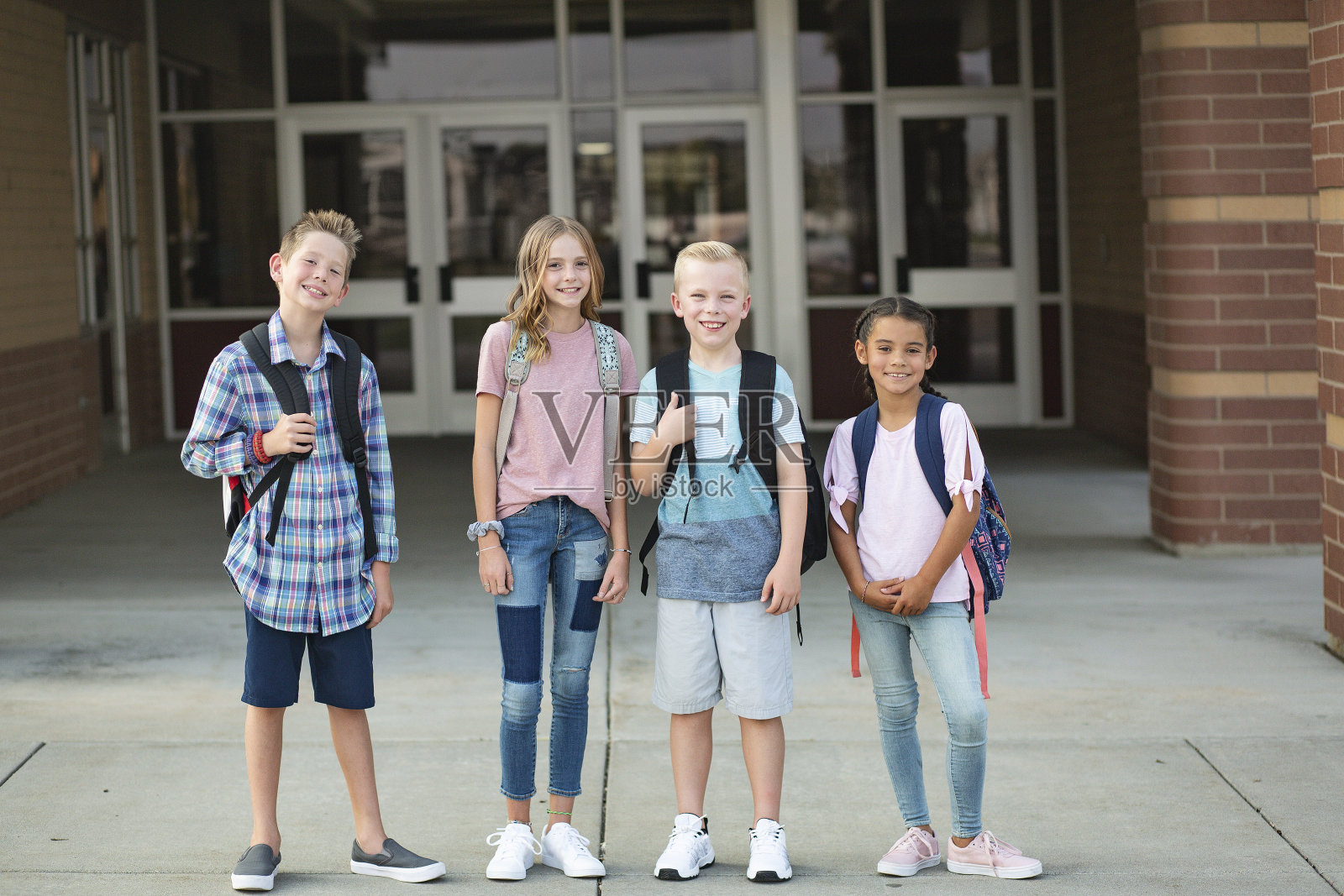 一群小学生站在他们的学校前面。微笑，放学后一起出去玩。照片摄影图片