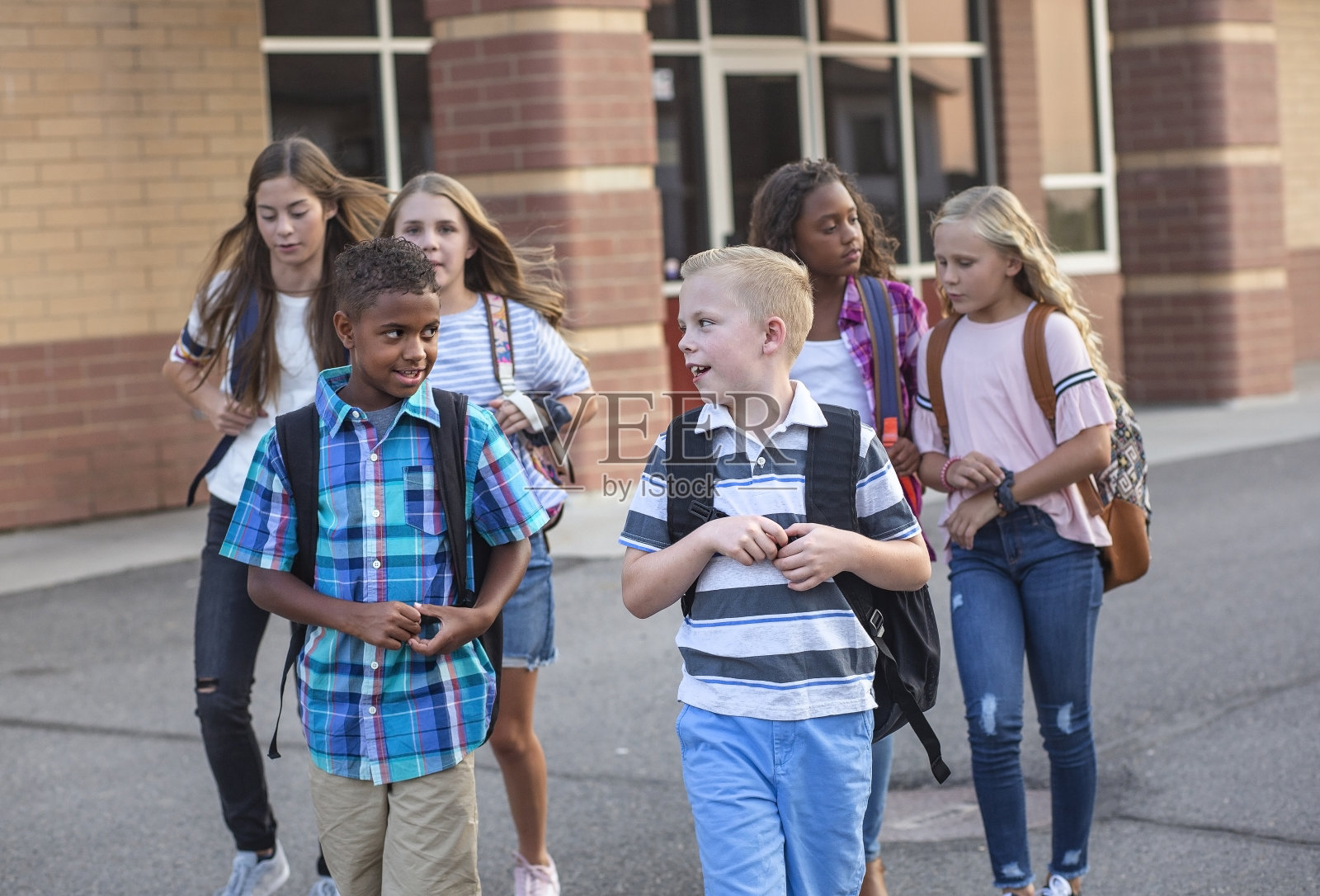 每天放学后，一大群形形色色的孩子离开学校。学校的朋友们一起散步，一起谈论着他们的青春期前的孩子们在学校大楼前微笑的照片照片摄影图片