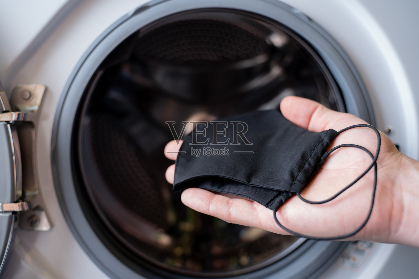 一个男人的手正把一个黑色的面罩扔进洗衣机照片摄影图片