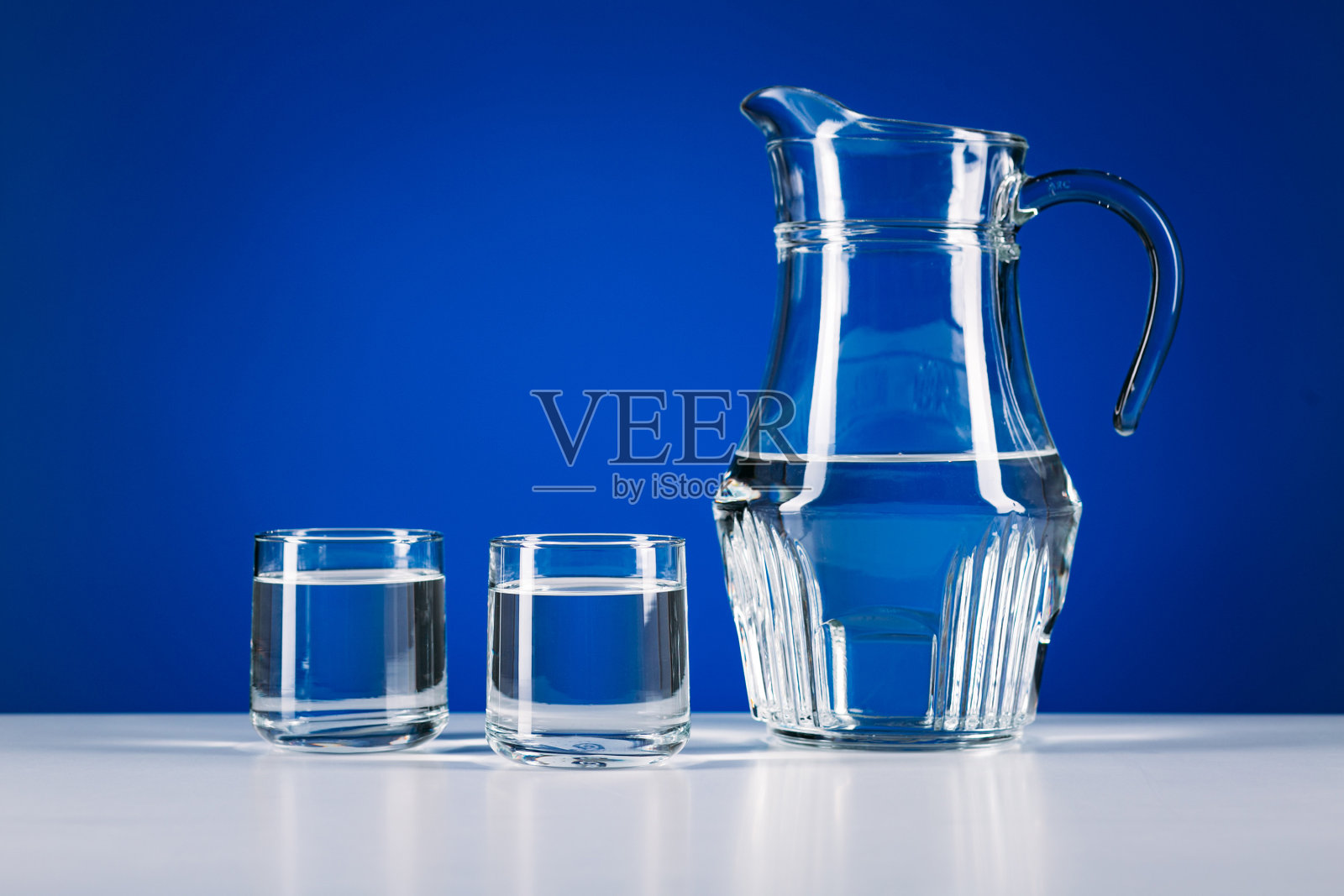 蓝色背景上的玻璃水罐和两个玻璃杯照片摄影图片