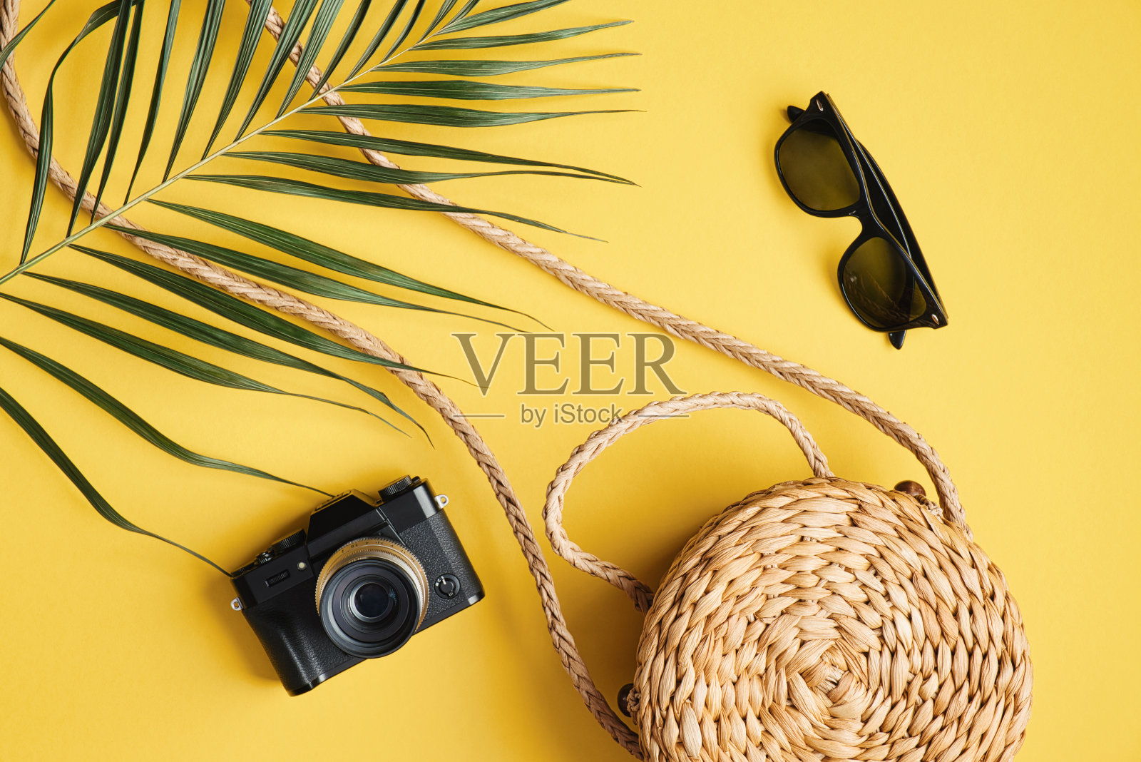 平铺旅行配件在黄色的背景。俯视图棕榈叶，藤草包，相机，太阳镜。旅行或度假的概念。夏季背景与时尚的女性服装照片摄影图片