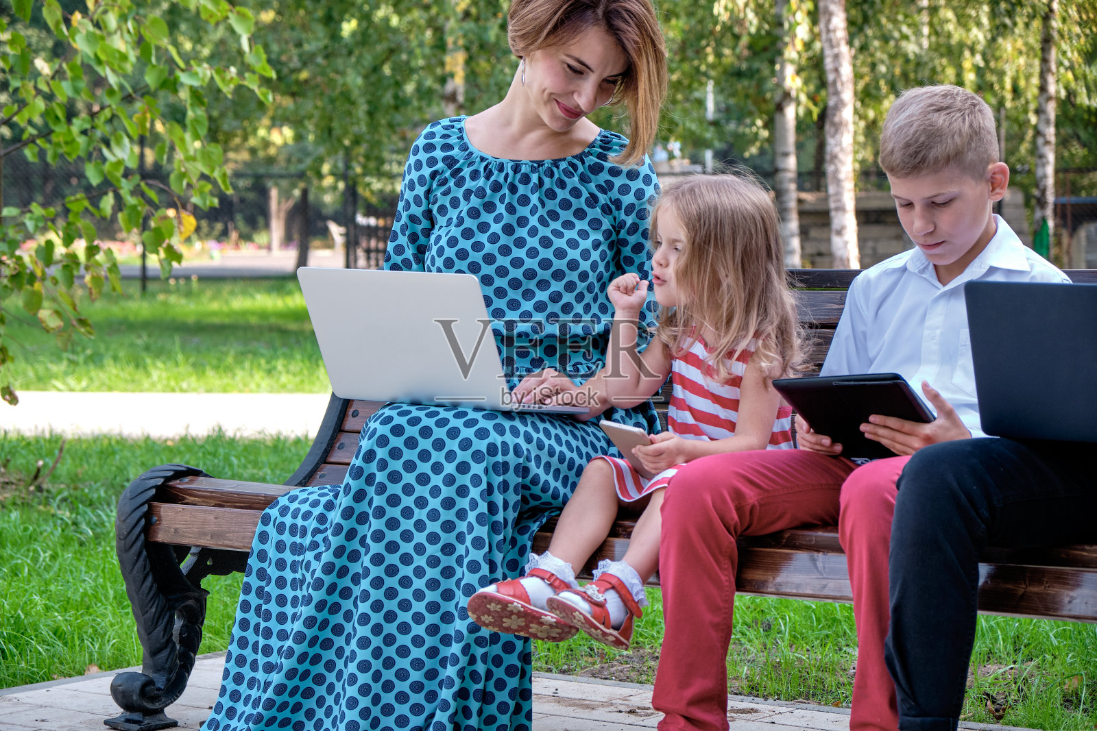 妈妈和孩子们坐在自然上使用平板电脑和智能手机。在现代生活中，家庭玩电脑或上网，电子设备和孩子照片摄影图片