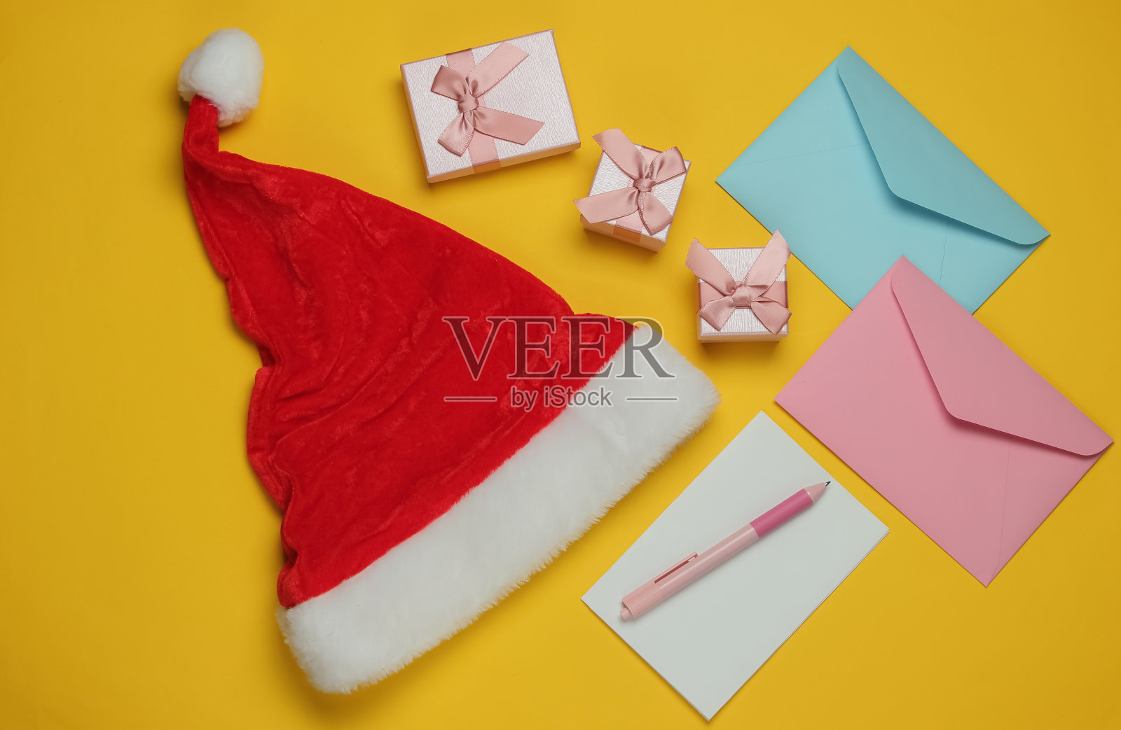 写给圣诞老人的信。圣诞老人的帽子，信封与信和笔，盒子的礼物在黄色的背景。圣诞节平。俯视图照片摄影图片