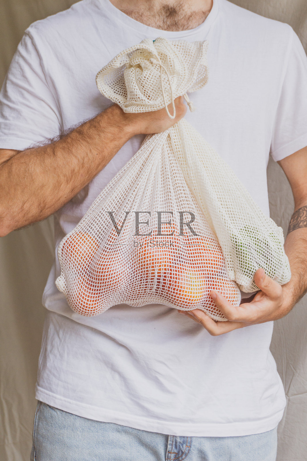 环保的生活方式和健康的饮食理念。一名男子手里拿着一个装着新鲜西红柿的可重复使用的网眼购物袋。照片摄影图片