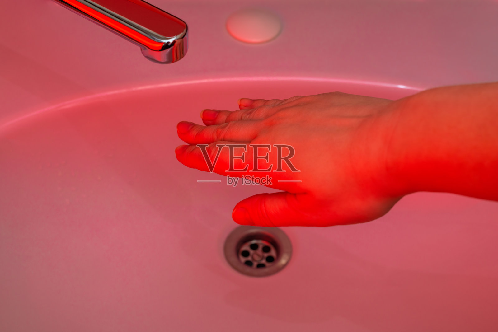 一只手伸向红色的水龙头。预防冠状病毒感染的卫生观念。红光沐浴照片摄影图片