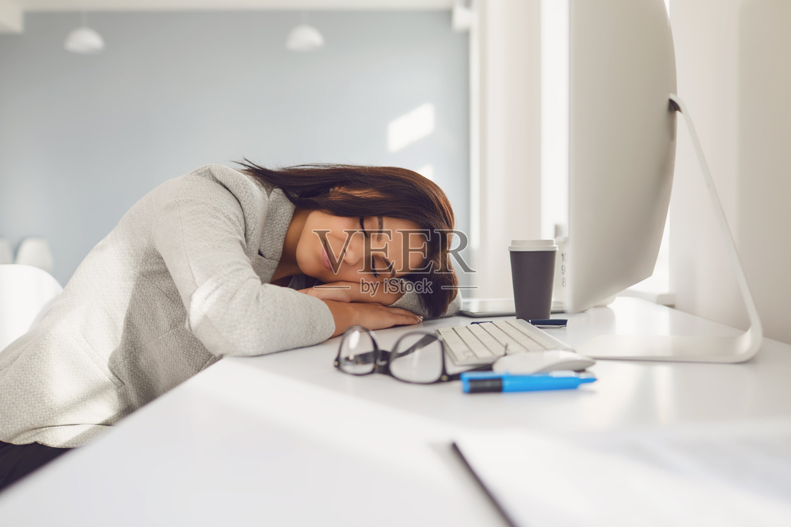 疲惫的女商人躺在办公室的办公桌上睡着了。照片摄影图片