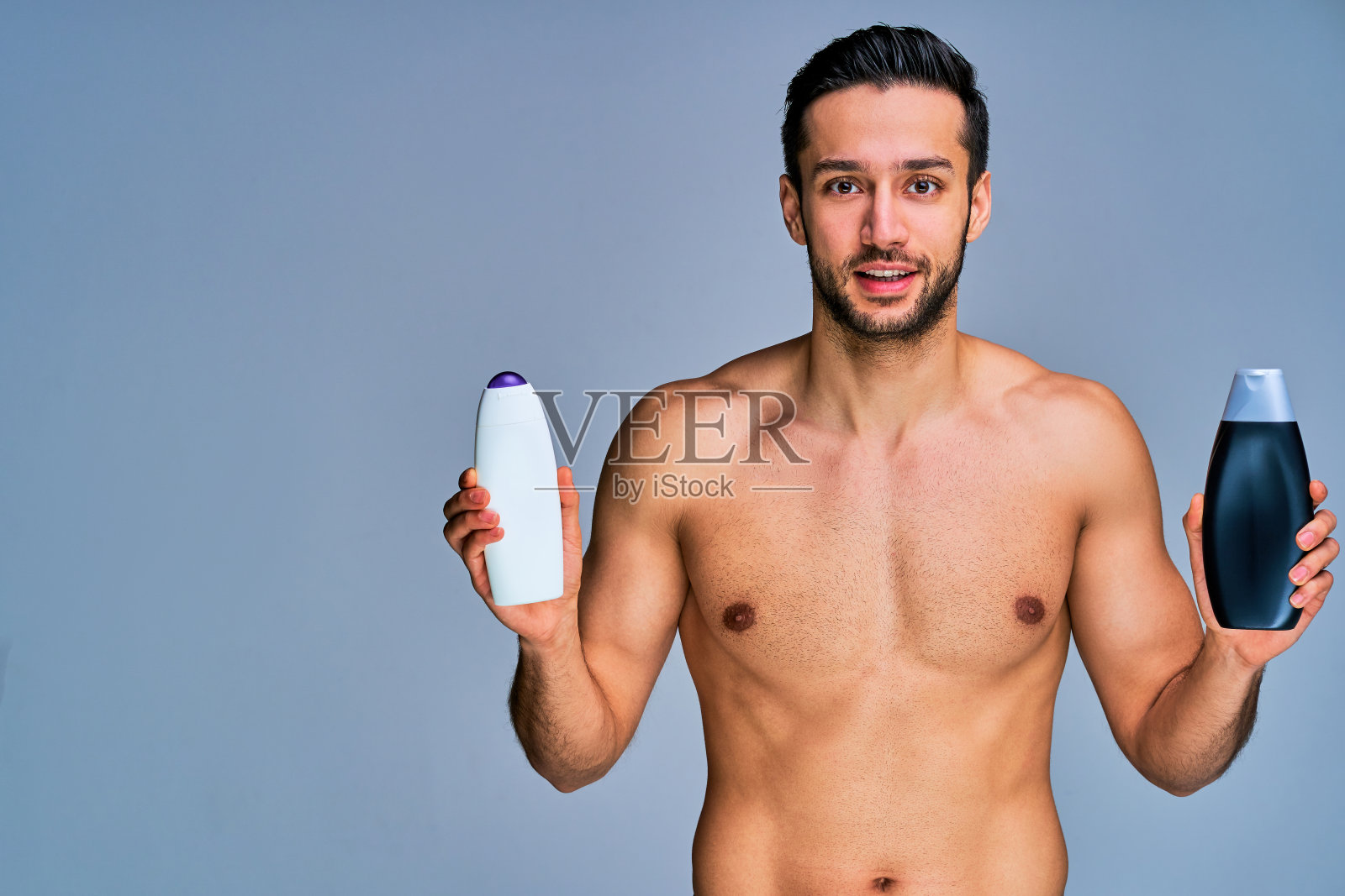 黑头发留胡子的快乐男人展示了洗发水瓶子。美丽的概念照片摄影图片