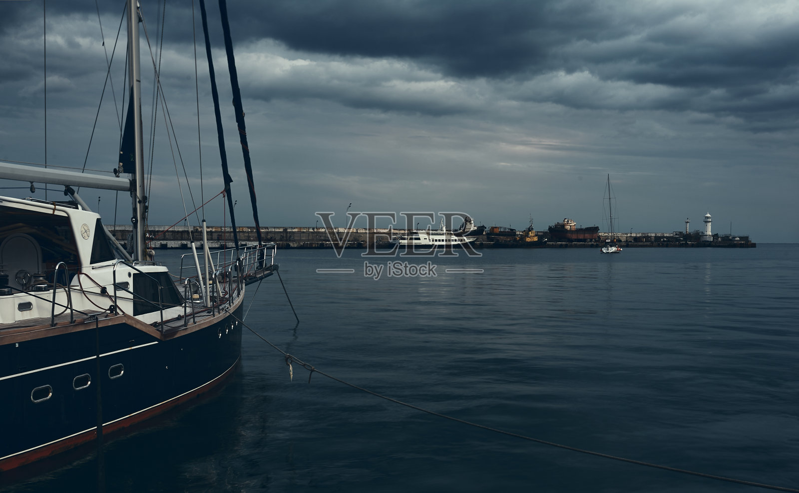 停泊在有灯塔的海湾里的帆船。照片摄影图片