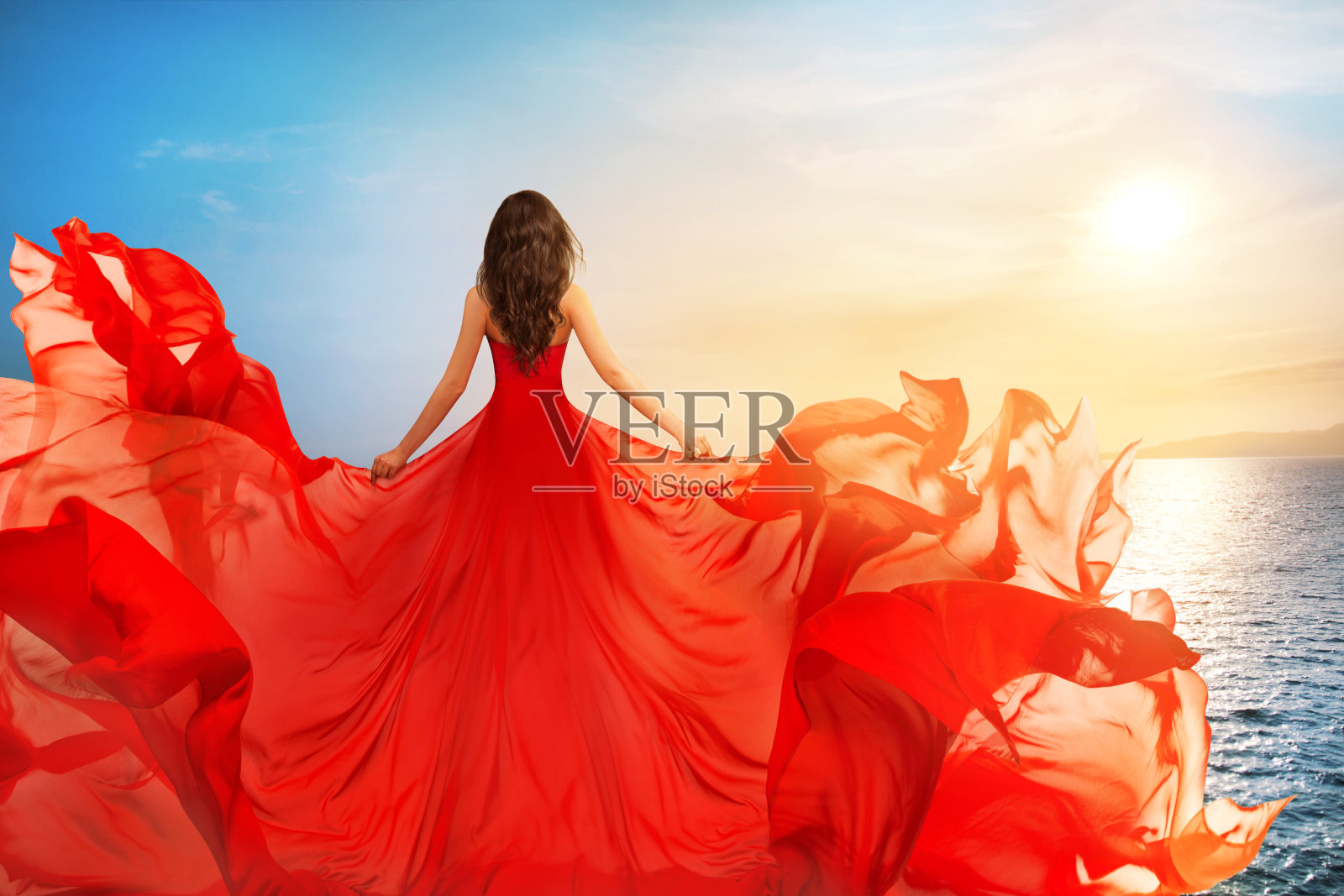 红色飞衣女子后视镜在风中飘扬，女孩在日落海上飘扬的长袍照片摄影图片
