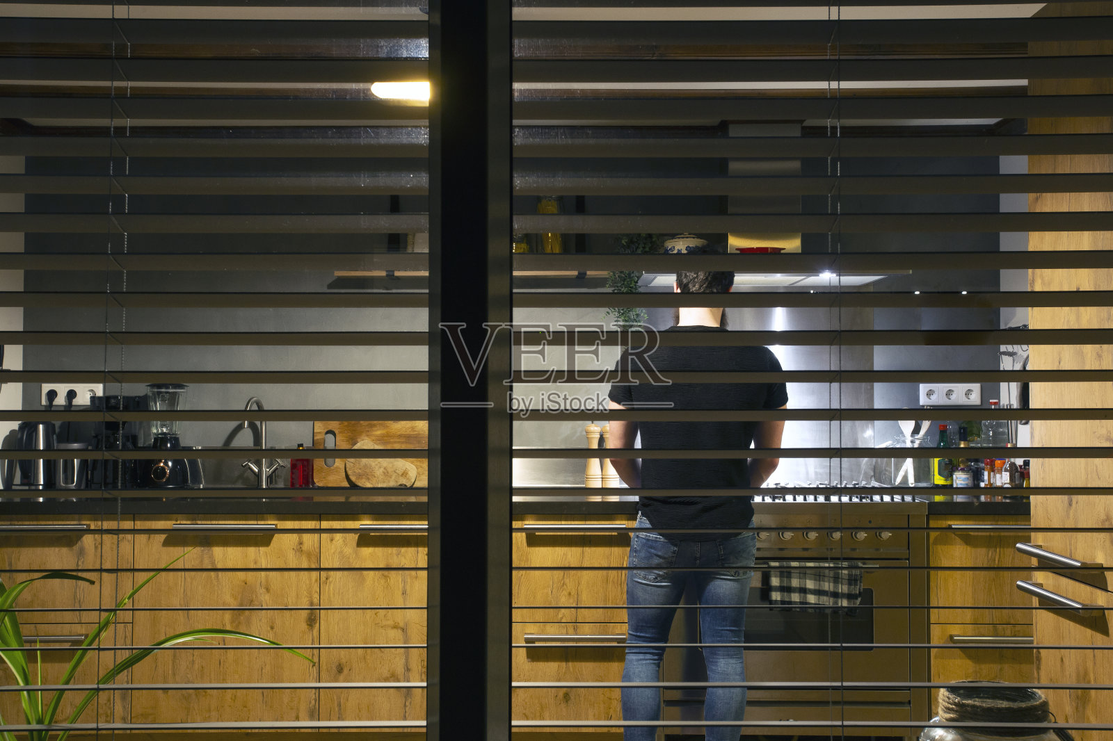 一个男人站在一个舒适的厨房做饭晚餐在晚上从窗外看，现代的内部照片摄影图片