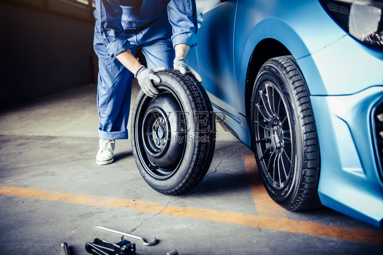 男机械师抱着滚动轮胎在修理厂维修背景。技术人员更换冬季和夏季轮胎，以确保行车安全。交通和汽车维修概念照片摄影图片