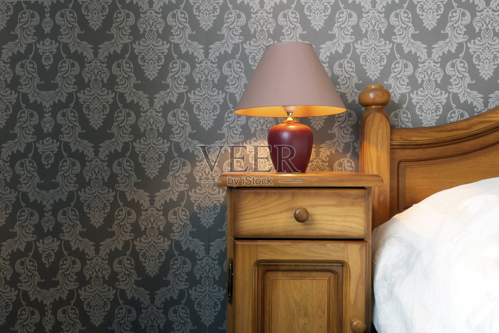 一张木床的特写，白色的床单和一个舒适的灯，图案墙纸复古设计。照片摄影图片