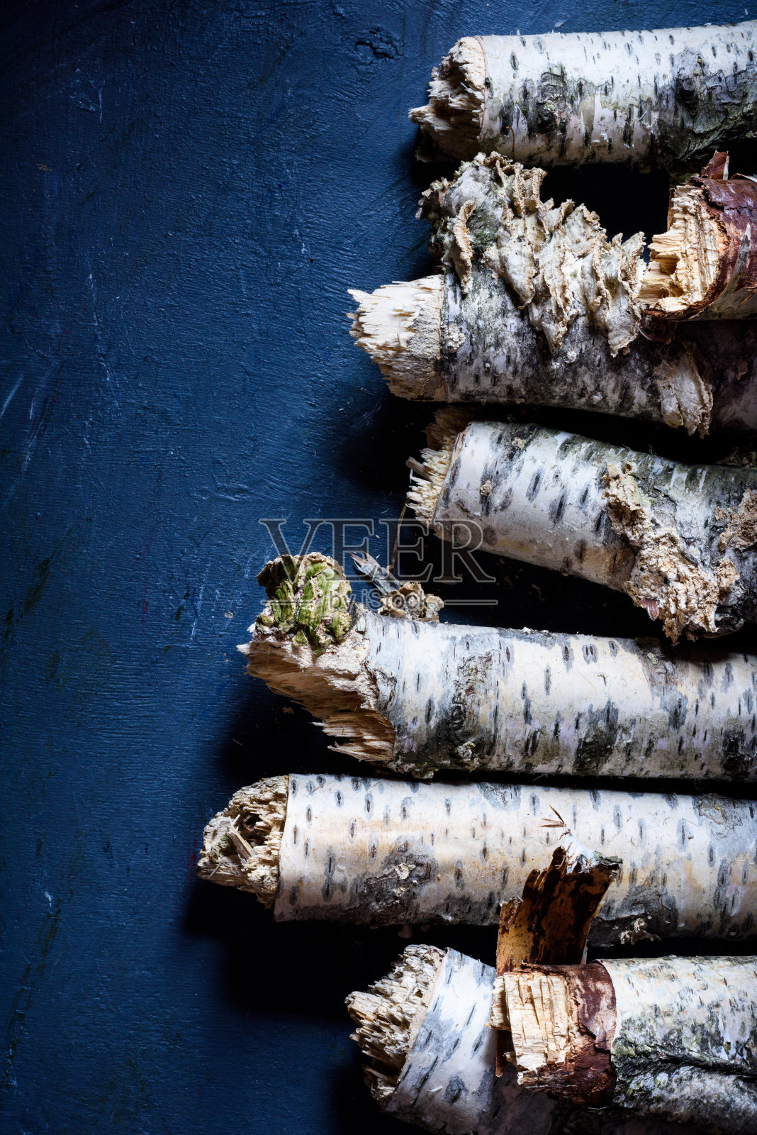 桦木柴火，原木堆放在蓝色的背景上，准备作壁炉用。照片摄影图片