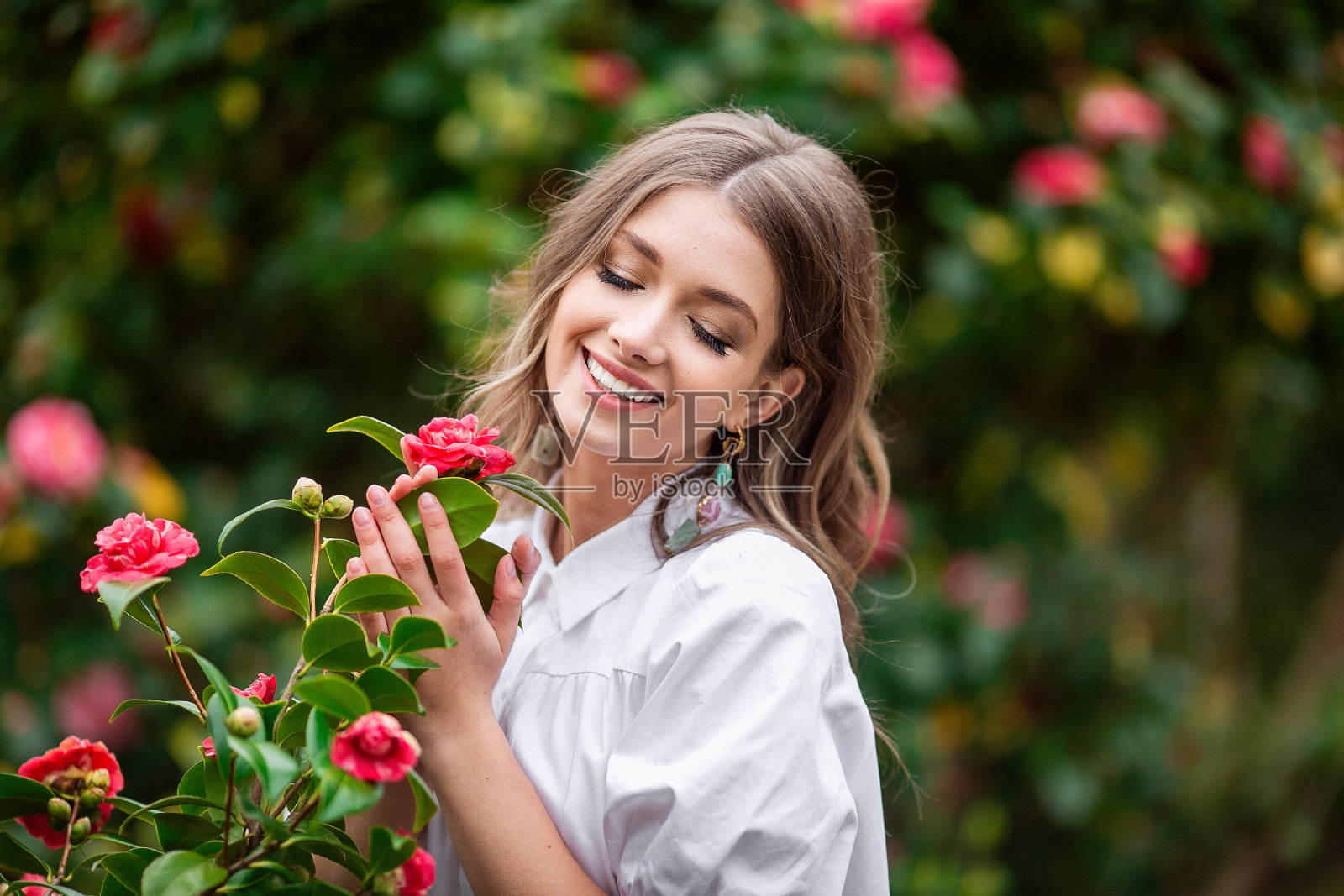 美丽的女人与春天盛开的粉红色的花。一个年轻的女孩微笑着欣赏粉红色的玫瑰花。夏季。照片摄影图片