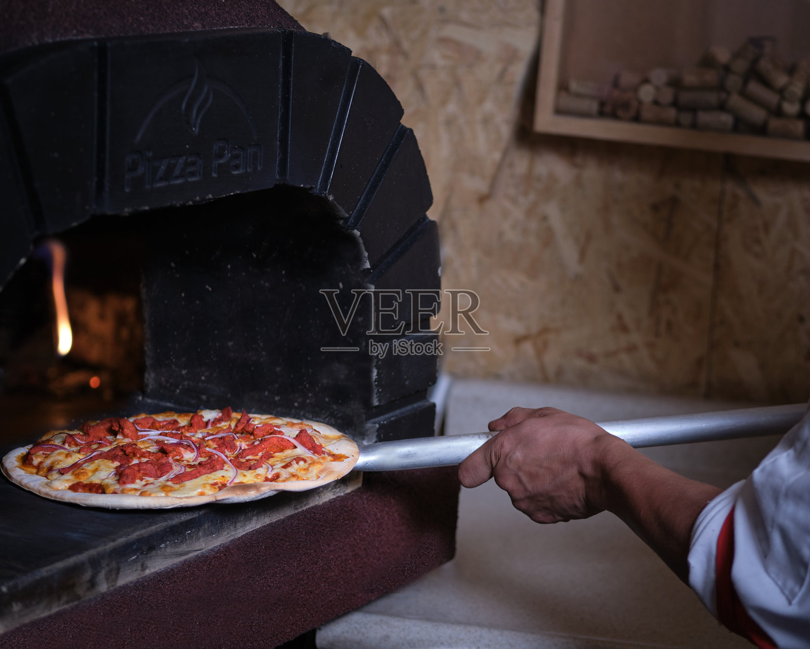厨师将披萨与柴火一起放入粘土烤箱照片摄影图片