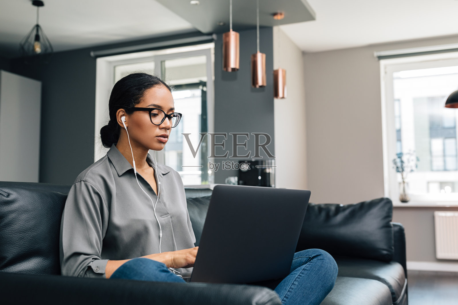 年轻女子在她的公寓工作。女性自由职业者坐在沙发上使用笔记本电脑。照片摄影图片
