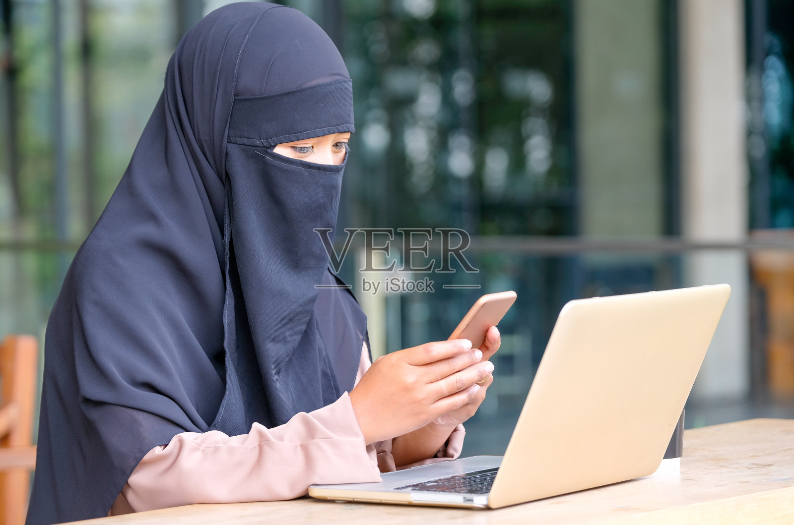一个穆斯林女孩在家里工作的时候用手提电脑在阳台上使用手机照片摄影图片