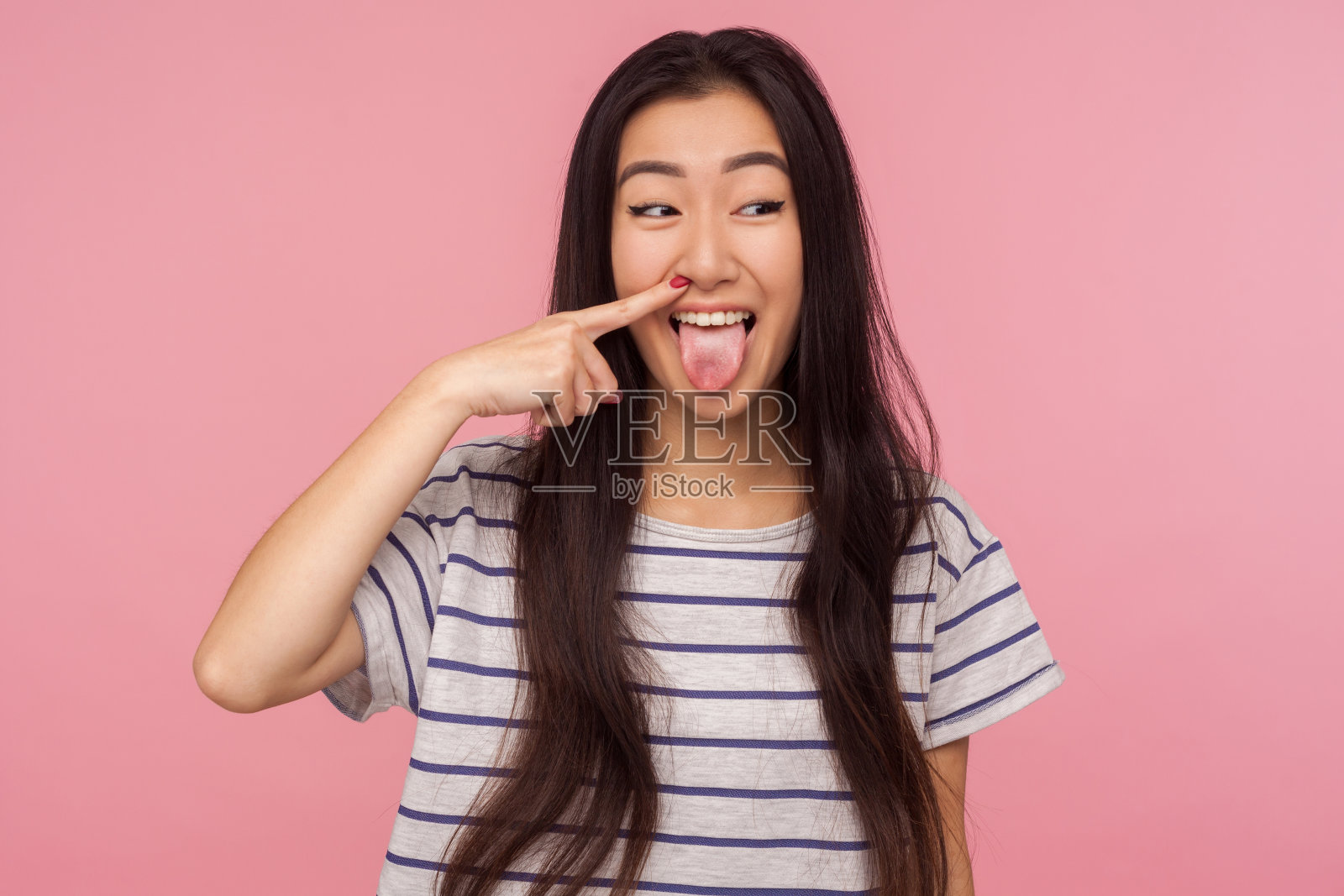 滑稽滑稽的长头发女孩的肖像，穿着条纹t恤挖鼻子，拉鼻屎和显示舌头照片摄影图片