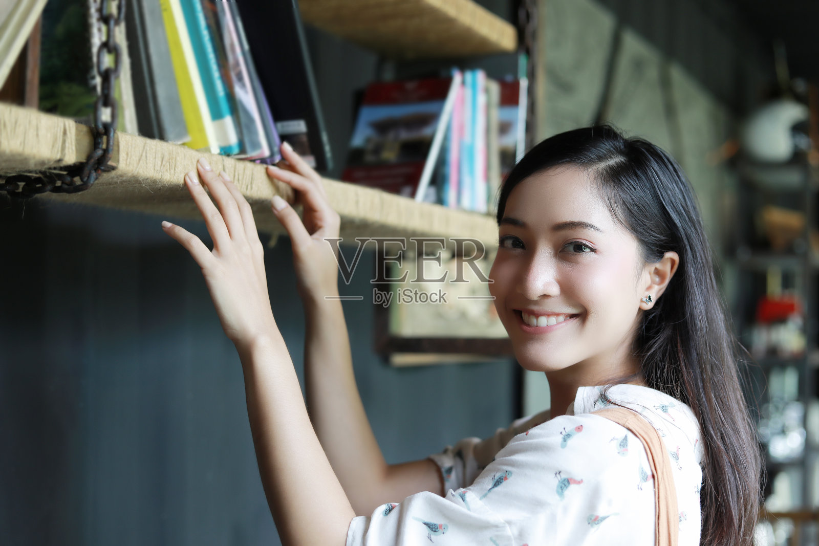一位可爱的亚洲妇女在书架上选了一本书，她笑着在家度假。照片摄影图片