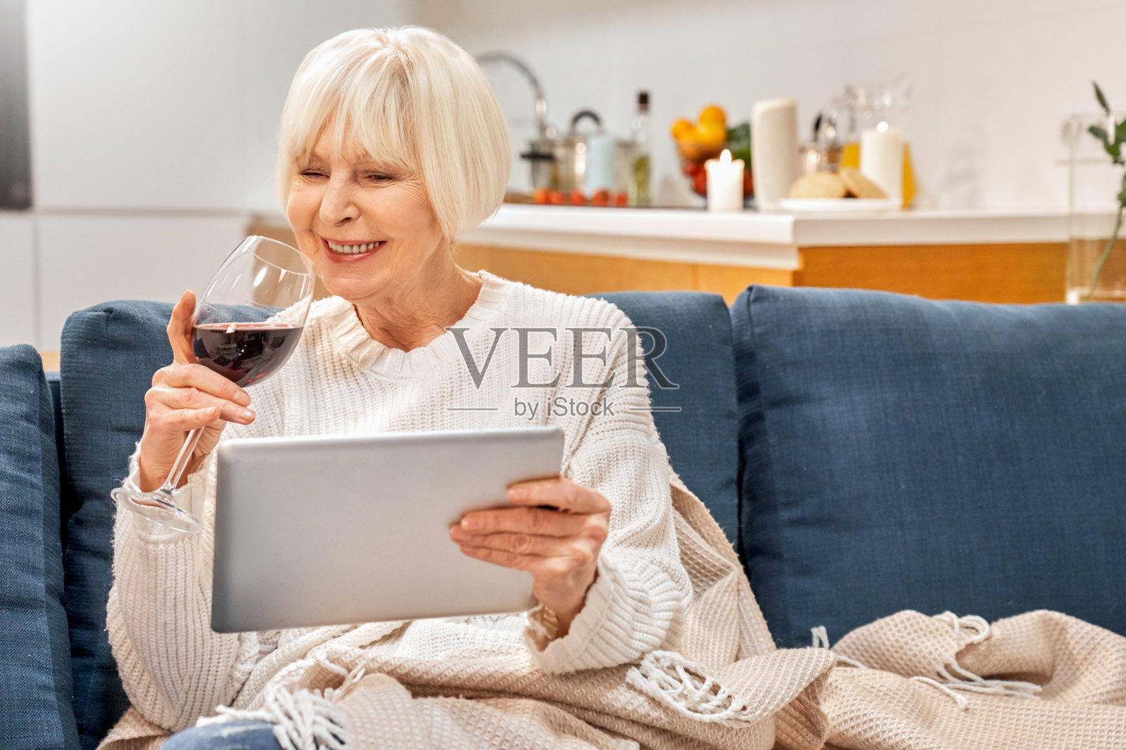 积极的70多岁的老美人舒适的家气氛放松享受喝红酒购物坐在沙发上使用现代设备平板电脑。微笑感觉快乐开朗健康的女士女性阅读看电影社交媒体照片摄影图片