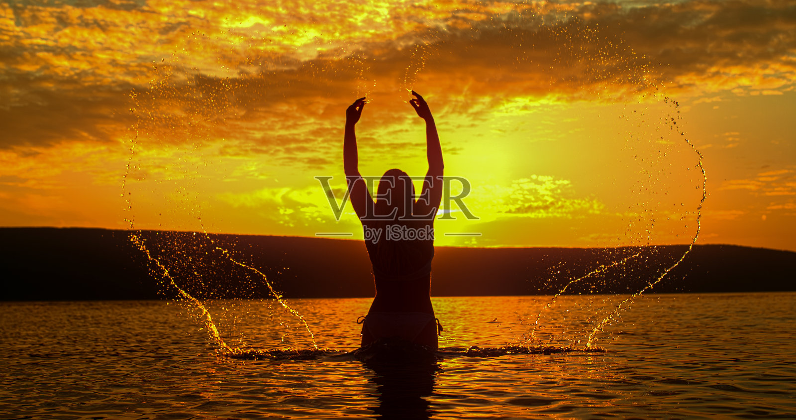 女人的剪影享受溅水在日落照片摄影图片