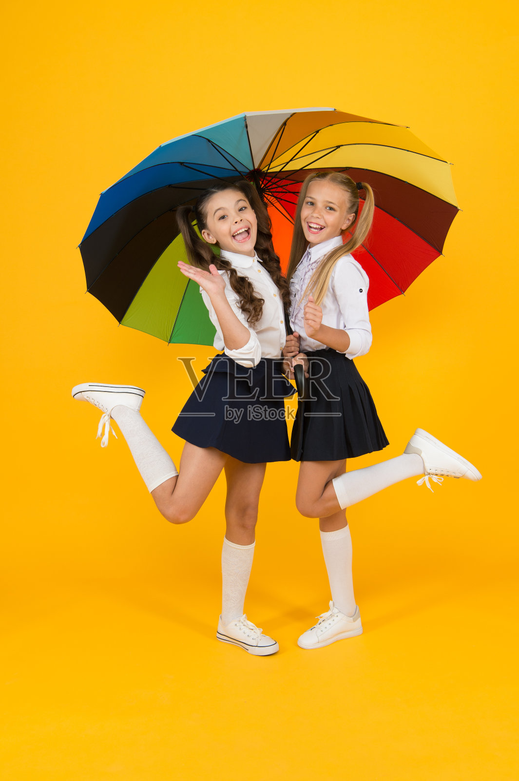 小学的时尚。快乐学校的孩子们拿着五颜六色的雨伞，穿着时尚。穿着正式制服的时尚小女孩在黄色背景下微笑。为小孩子设计的学校时装照片摄影图片