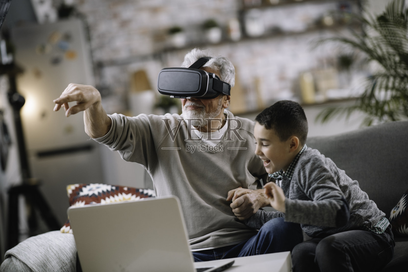 孙子和爷爷在家里的沙发上玩VR。照片摄影图片