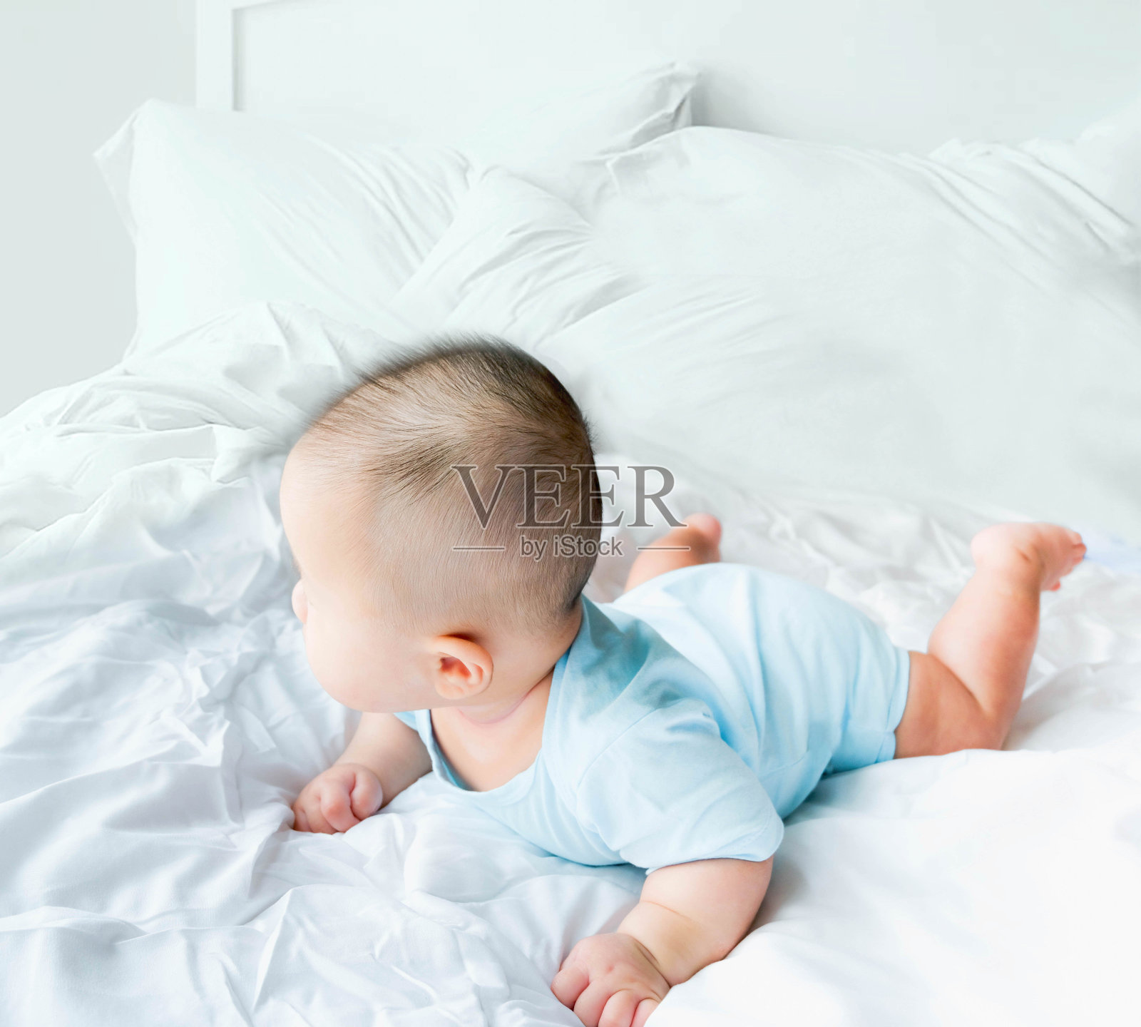一个刚出生的亚洲可爱男婴穿着蓝色婴儿紧身衣在床上爬行，可爱的胖宝宝5个月大享受和快乐，柔软的选择性焦点照片摄影图片