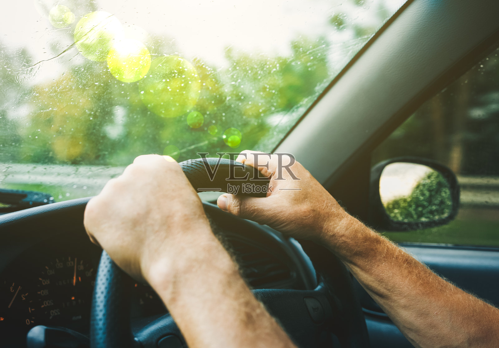 男人手拉着汽车的方向盘。雨点落在挡风玻璃上。那家伙在恶劣的天气里旅行。危险的条件。生活方式的概念。照片摄影图片