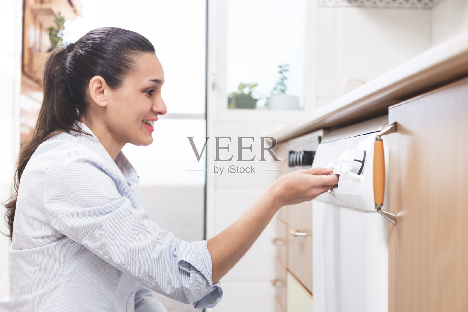 快乐的年轻白人女人，打开她公寓厨房里的洗碗机。做家务的概念。照片摄影图片