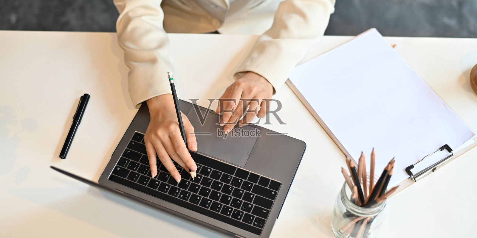 俯视图的形象，女商人的手打字的笔记本电脑，放在白色的工作桌上，周围的钢笔，铅笔在花瓶和剪贴板。有序的工作空间的概念。照片摄影图片