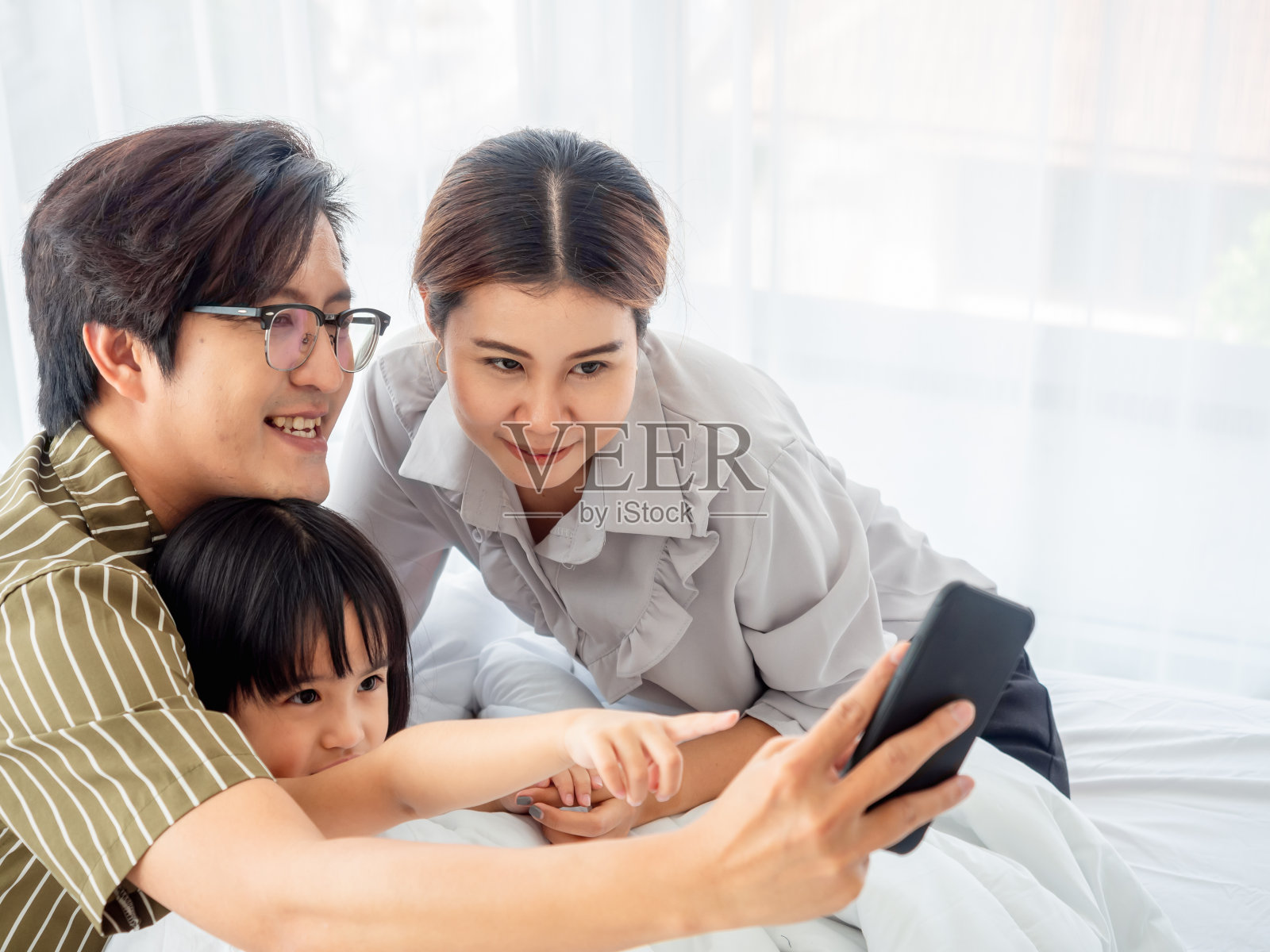 幸福家庭在卧室的概念。父亲坐在地板上用笔记本电脑，母亲和女儿躺在卧室的床上。照片摄影图片