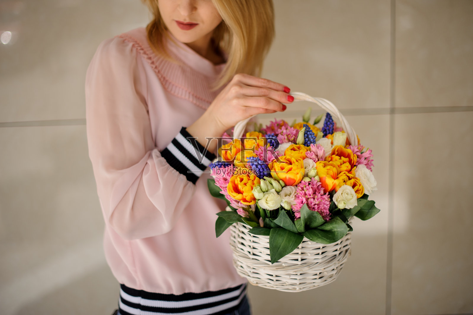 女人手里拿着一个装饰用的篮子，里面装着各种各样的春花。照片摄影图片