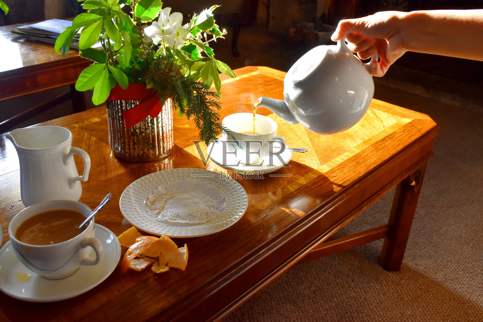 把热茶倒进一个杯子里，在木头桌子的背景下有明亮的阳光，传统的英国下午茶。照片摄影图片