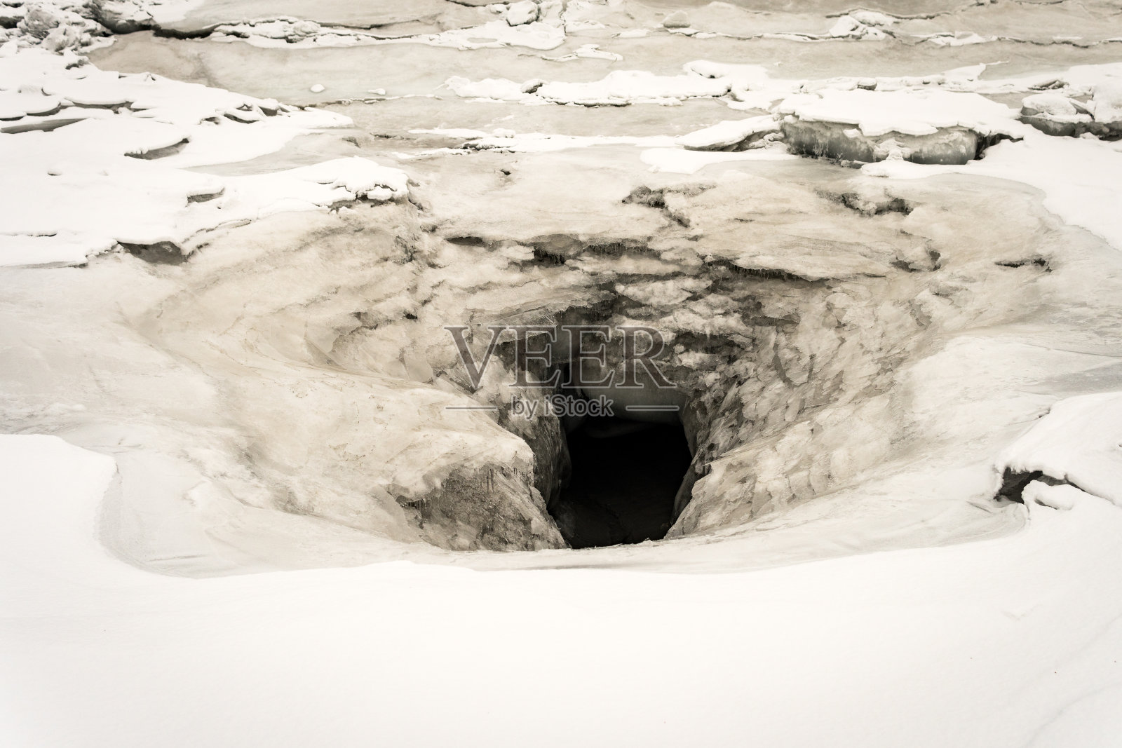 结冰的河流上的大洞。地上覆盖着雪的洞穴入口。阿拉斯加安克雷奇北部一条结冰的小溪上的冰正在破裂、融化。照片摄影图片