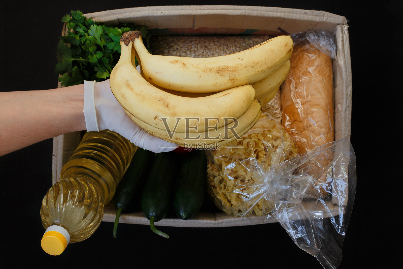 瓦兰特戴着防护手套将盒子装满了食物，背景是黑色的。捐赠的概念。照片摄影图片