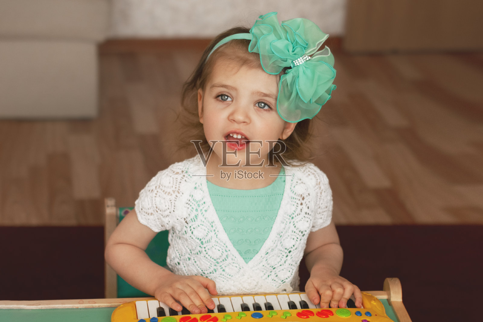 欢快的女孩的肖像，弹奏儿童钢琴和唱歌，穿着绿色的裙子，白色的花边和蝴蝶结在她的头选择性的焦点照片摄影图片