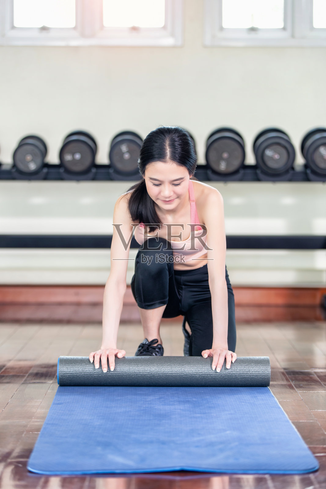 在健身房上瑜伽课前，一个女人在滚动她的垫子。照片摄影图片