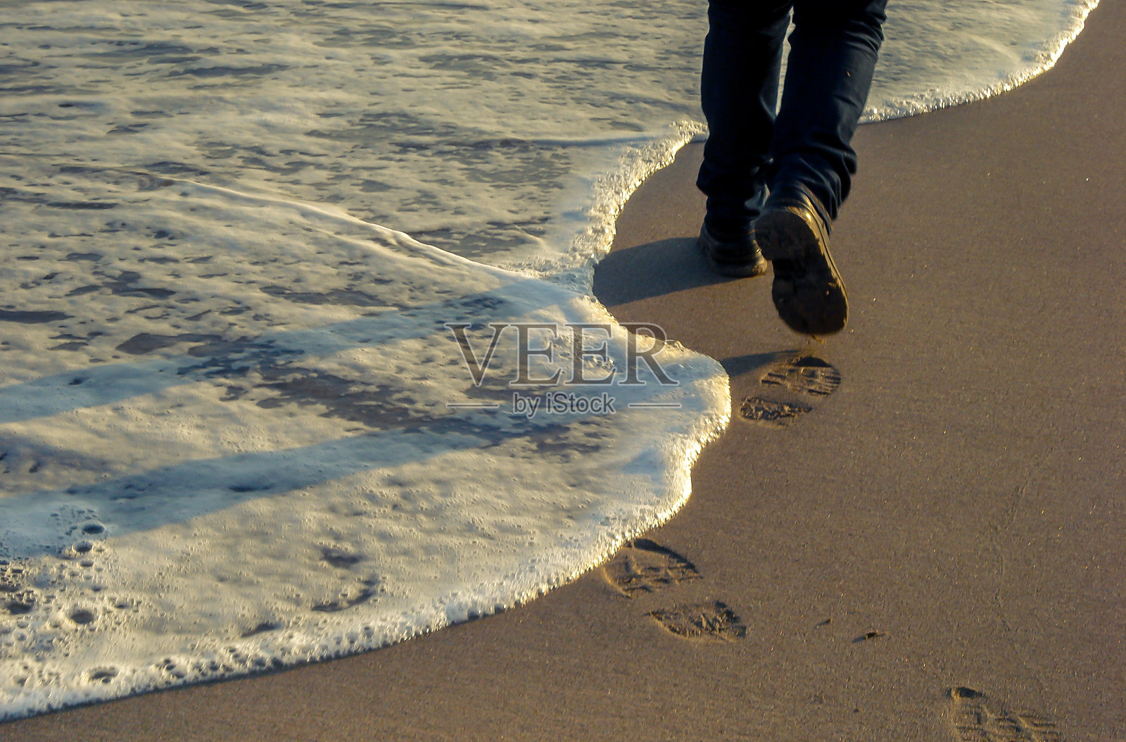浪沫海浪到达海岸或海滩时产生的泡沫穿着靴子的女人走在沙滩上，在水边留下脚印。B照片摄影图片