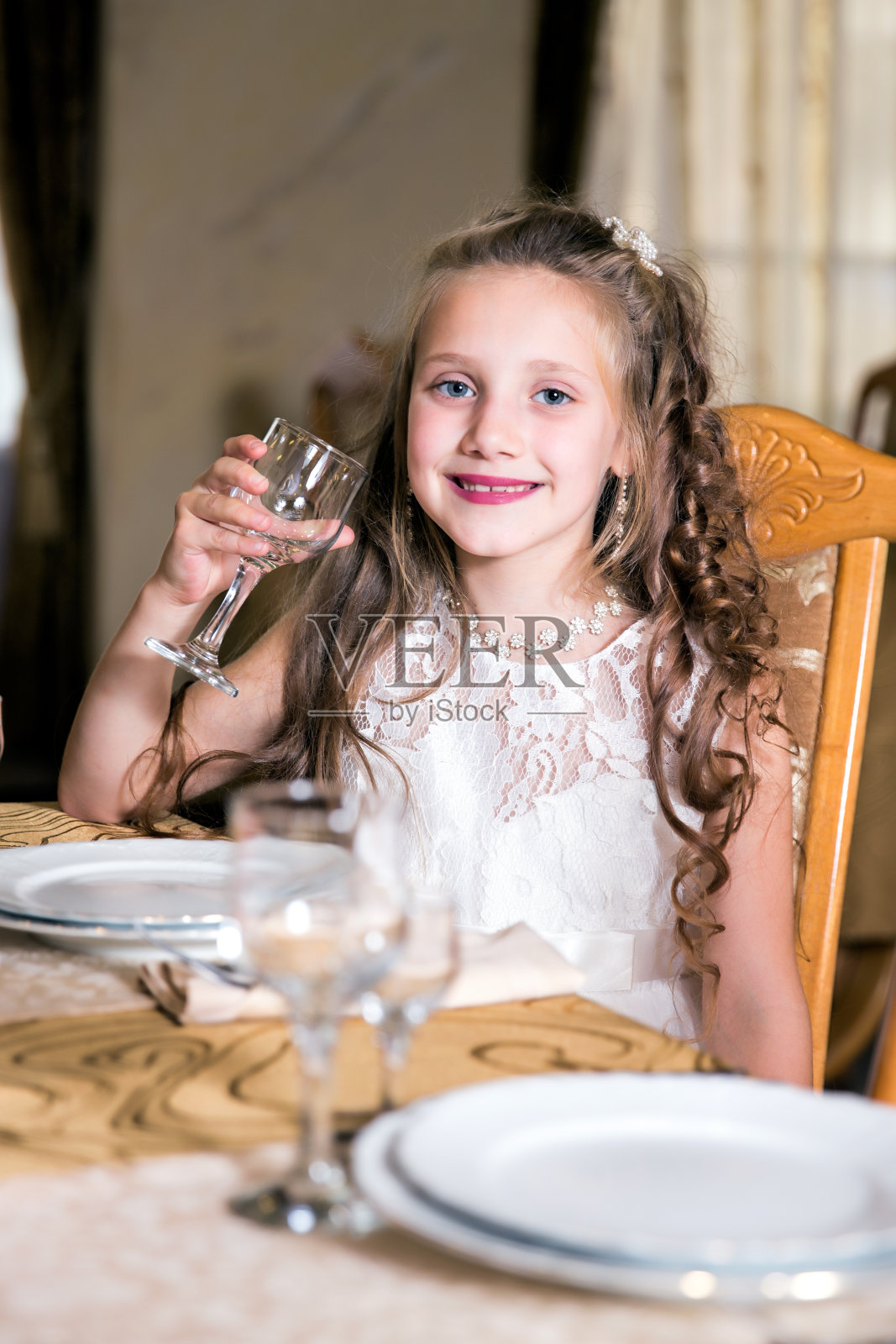 穿着白色连衣裙的可爱女孩坐在节日的餐桌旁照片摄影图片