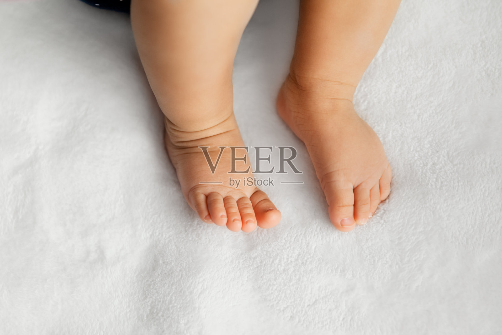 婴儿的腿放在柔软的白色毯子上作为背景，在自然光下，婴儿的脚照片摄影图片