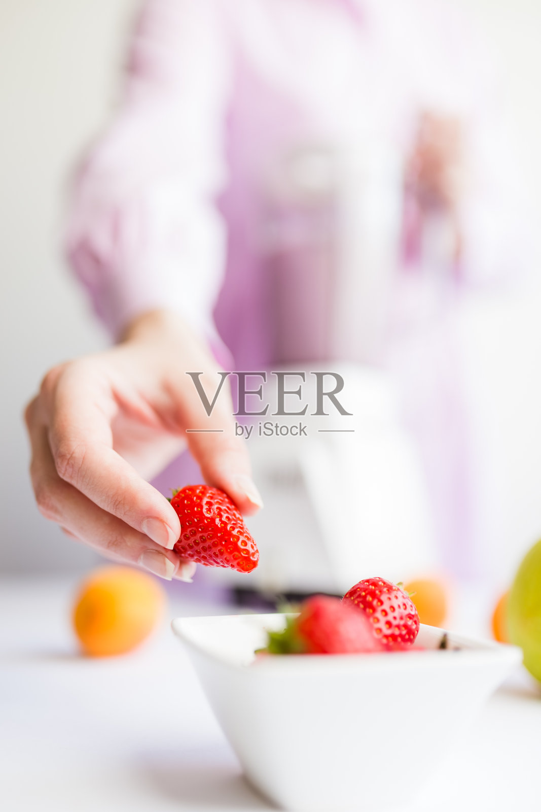 在厨房里拿着草莓准备水果奶昔的女人。照片摄影图片