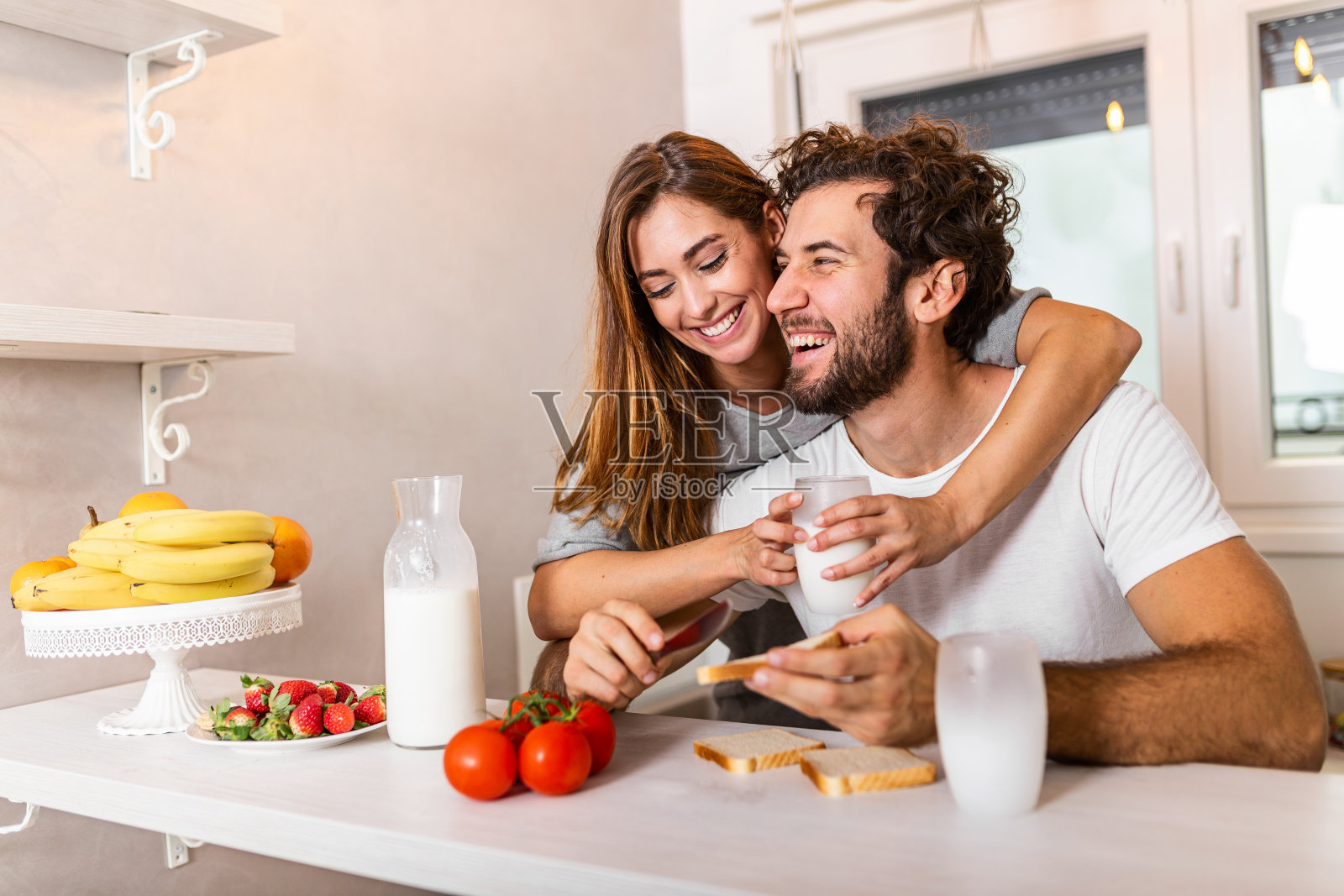 快乐的年轻夫妇在现代的厨房室内，同时准备新鲜的水果和蔬菜食物沙拉。美丽的年轻夫妇谈笑风生，在厨房里做着健康的食物。照片摄影图片