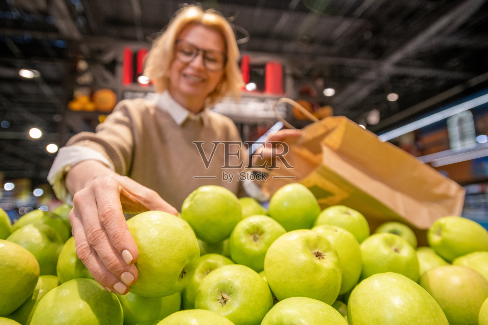 金发成熟的女顾客带着纸袋选择新鲜的青苹果照片摄影图片