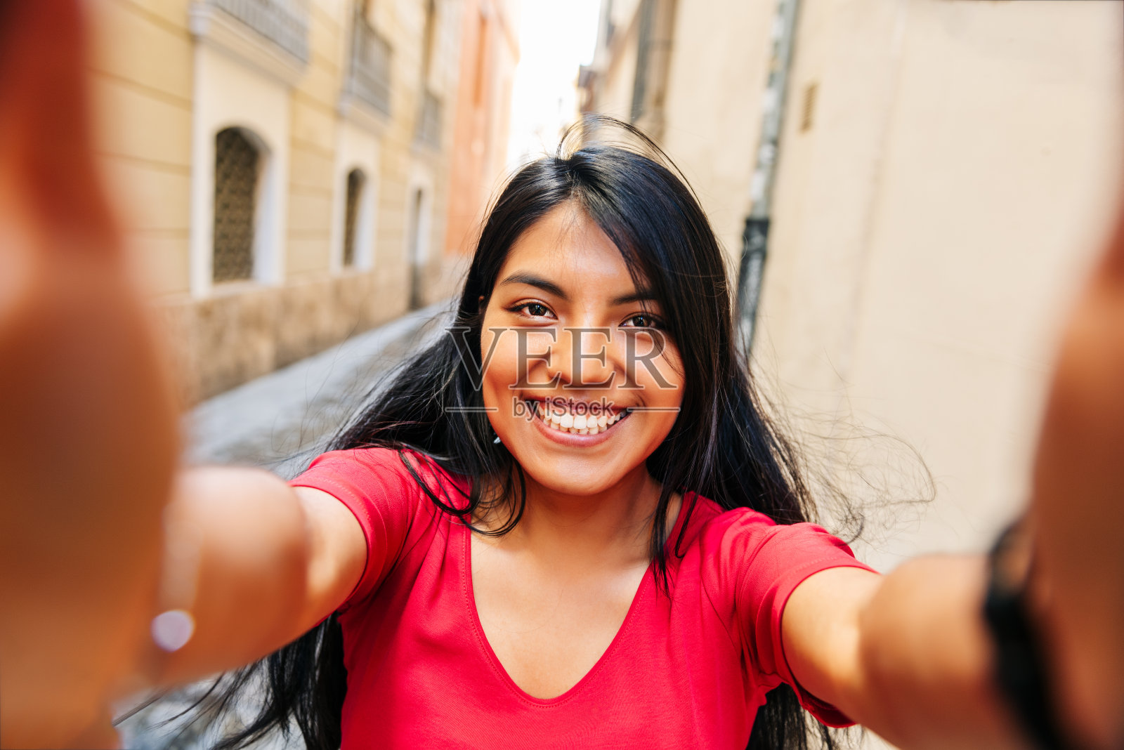 近距离自拍的黑发拉丁女孩微笑着双手拿着相机，在欧洲城市的街道上照片摄影图片
