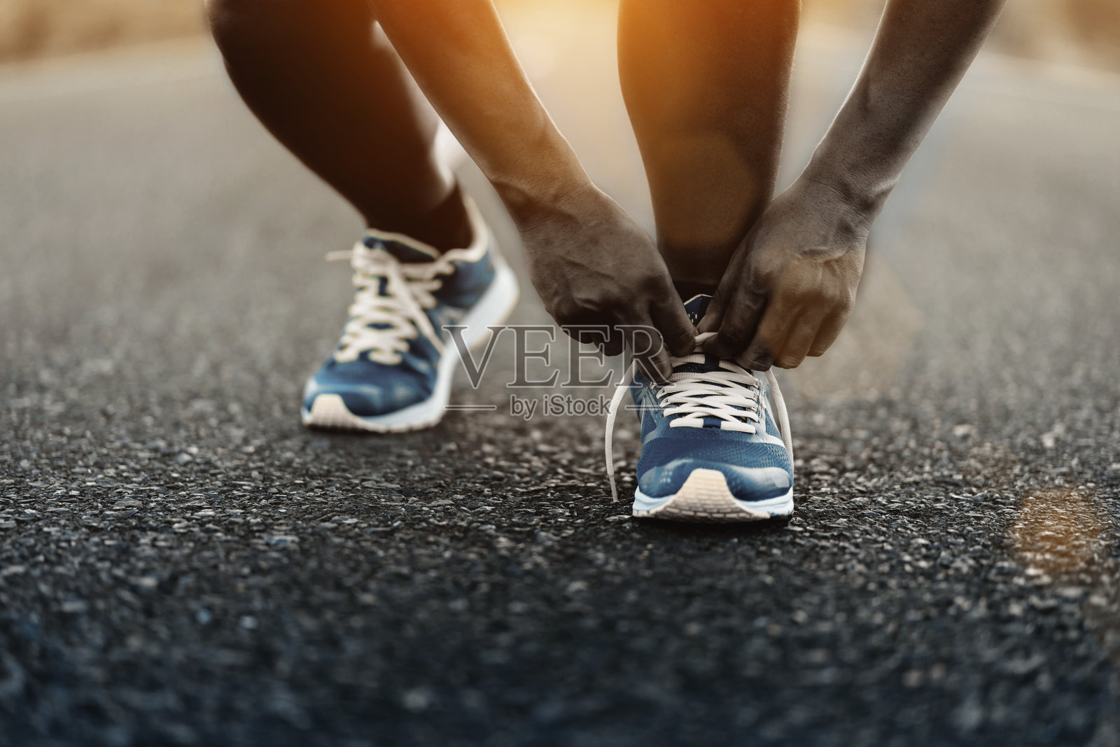 年轻的非洲裔美国男子在户外的道路上系鞋带跑步。照片摄影图片